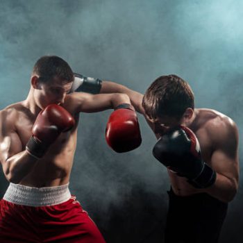 Two professional boxer boxing on black smoky studio background.